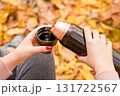 Female hands holding a thermos of hot tea against the background autumn leaves 131722567