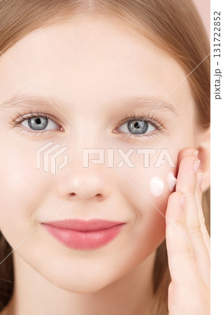 Close-up portrait of a smiling cheerful girl applying face cream on cheek for skin glow. Gen Alpha. Ad face cream and skincare products for teens. Self care. Blonde girl with blue eyes. Studio shot Close-up portrait of a smiling cheerful girl applying face cream on cheek for skin glow. Gen Alpha. Ad face cream and skincare products for teens. Self care. Blonde girl with blue eyes. Studio shot 131722852