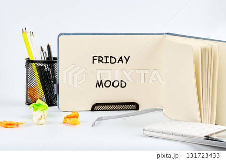 A notepad reads FRIDAY MOOD on a work desk. Crumpled papers suggest a long week. Office supplies and a notebook complete this relatable lifestyle scene 131723433