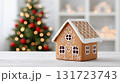 Gingerbread house decorated with icing sits on a wooden table with a festive Christmas tree in the background, creating a warm holiday atmosphere 131723743