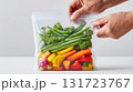 Hands hold a reusable silicone food pouch filled with colorful, fresh vegetables like bell peppers, green beans, and parsley. 131723767
