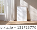 Bright and airy room with a blank frame foe wall art mockup leaning against the wall illuminated by natural sunlight filtering through sheer curtains 131723770
