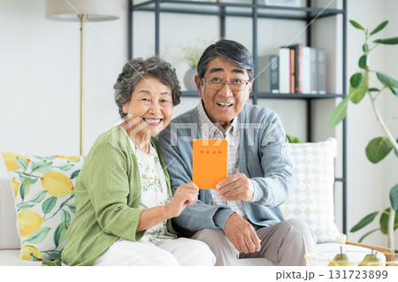 リビングで年金手帳を持つシニアの夫婦 131723899