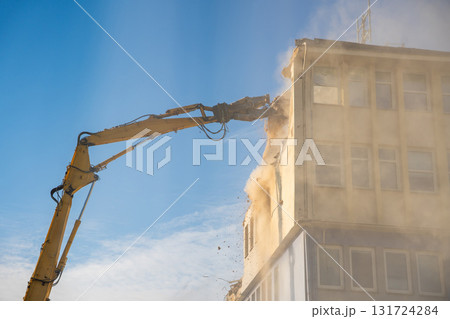 Powerful demolition of a concrete office building with a yellow high-reach excavator. Concept of transformation, destruction and construction renewal. 131724284