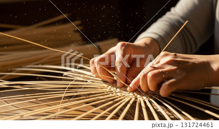 Skilled artisan hands weaving traditional bamboo basket with natural reed strips in workshop with warm golden lighting and floating dust particles 131724461