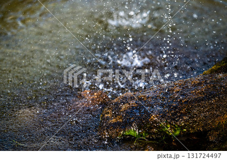 close-up view of water splashing over a rock in a pool under a fountain 131724497