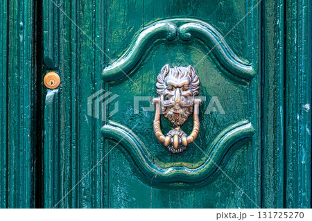 door knocker like antique head on the entrance of a house, Old ornate metal door handle 131725270