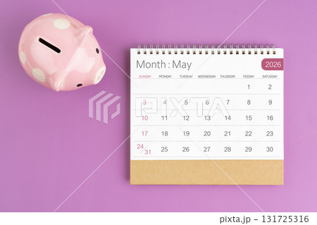 May 2026 desk calendar and pink piggy bank on purple background. May 2026 desk calendar and pink piggy bank on purple background. 131725316