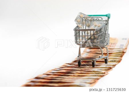 shopping cart full of pills on the road from fifty-euro banknotes, isolated on white, copy space 131725630