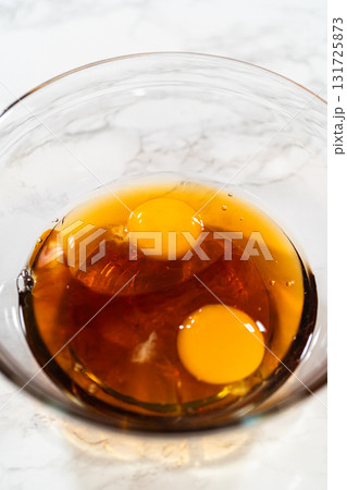 Close-up view of a glass bowl containing two eggs and maple syrup for the Chocolate Ginger Sugar Cookie Dough, creating the wet mixture base. Close-up view of a glass bowl containing two eggs and maple syrup for the Chocolate Ginger Sugar Cookie Dough, creating the wet mixture base. 131725873
