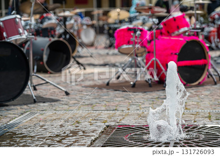 closeup of a fountain on the background of a defocused paved area with many drum kits closeup of a fountain on the background of a defocused paved area with many drum kits 131726093