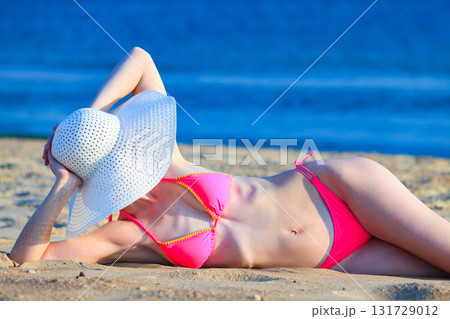 Woman in big straw sunhat sunbathing on a sandy beach. Summer holidays concept 131729012