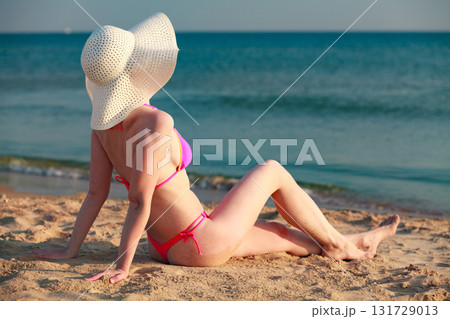 Woman in big straw sunhat sunbathing on a sandy beach. Summer holidays concept 131729013