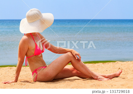 Woman in big straw sunhat sunbathing on a sandy beach. Summer holidays concept Woman in big straw sunhat sunbathing on a sandy beach. Summer holidays concept 131729018