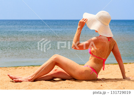 Woman in big straw sunhat sunbathing on a sandy beach. Summer holidays concept 131729019