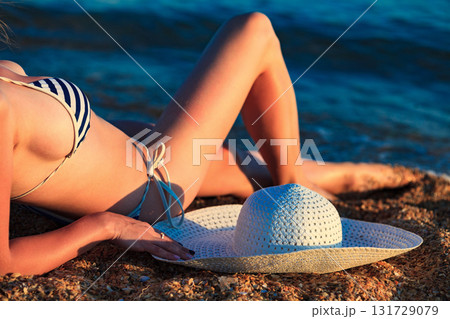Woman with a big straw sunhat sunbathing on a sandy beach. Summer holidays concept Woman with a big straw sunhat sunbathing on a sandy beach. Summer holidays concept 131729079