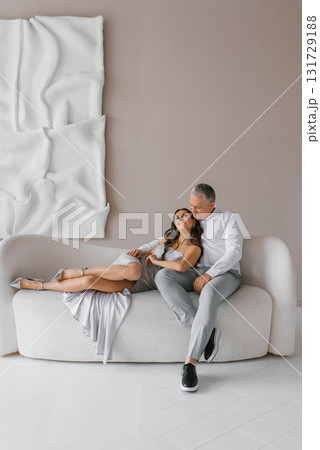 Man and woman are sitting on a white couch, embracing each other. Scene is warm and affectionate 131729188