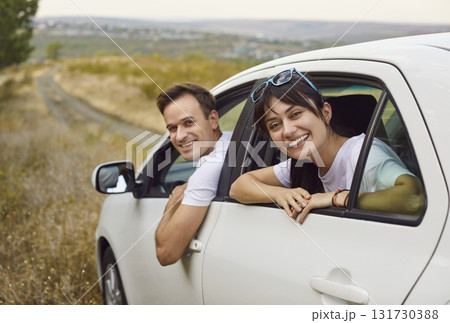 Happy couple waving from rental car during weekend road trip on scenic countryside Happy couple waving from rental car during weekend road trip on scenic countryside 131730388