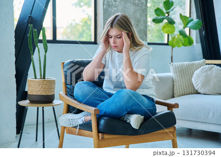 Unhappy upset young woman having headache, sitting in chair at home Unhappy upset young woman having headache, sitting in chair at home 131730394