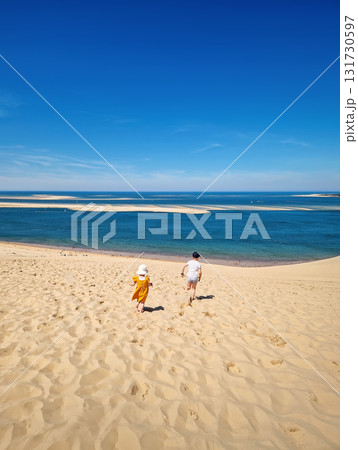 Two children, a girl and a boy run down a massive sandy hill toward the vast blue ocean. Wonderful scene of travel adventures at Dune of Pilat, La Teste-de-Buch, Arcachon Bay, France Two children, a girl and a boy run down a massive sandy hill toward the vast blue ocean. Wonderful scene of travel adventures at Dune of Pilat, La Teste-de-Buch, Arcachon Bay, France 131730597