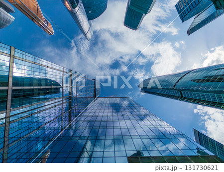 Urban canyon of glass skyscrapers reaching skyward under bright blue sky from street level view 131730621