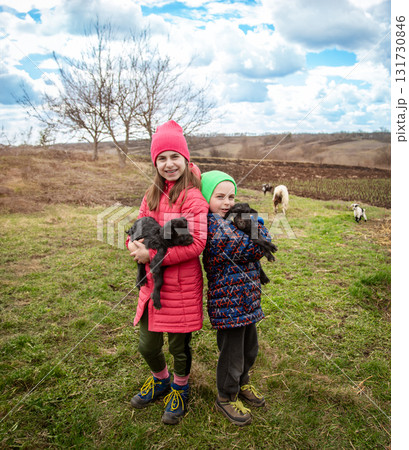 Joyful boy and smiling girl holding black goats on the farm. Rural lifestyle, childhood and animal care in the countryside. Joyful boy and smiling girl holding black goats on the farm. Rural lifestyle, childhood and animal care in the countryside. 131730846