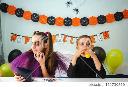 Two kids getting ready for Halloween. One girl applies makeup while boy inflates balloon. 131730869