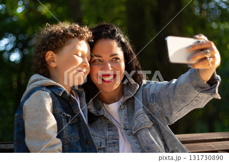 Young Caucasian mother and playful adorable little kid son making selfie photo or recording funny video, entertaining in public park Young Caucasian mother and playful adorable little kid son making selfie photo or recording funny video, entertaining in public park 131730890