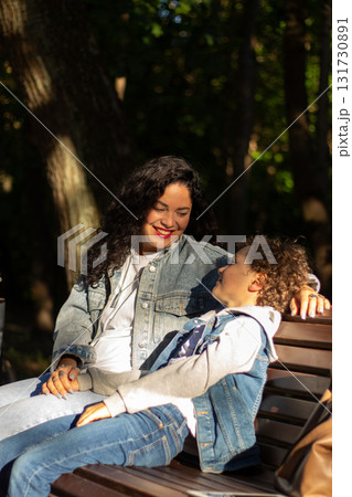 Portrait of young Caucasian single mother hugging her cute small son outside in park spending time on summer day together. Motherhood concept. Portrait of young Caucasian single mother hugging her cute small son outside in park spending time on summer day together. Motherhood concept. 131730891