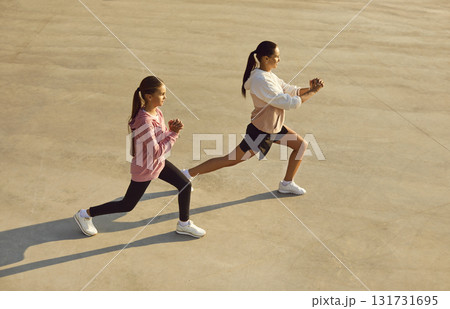 Mother and daughter doing fitness exercises during outdoor workout on city sports ground 131731695