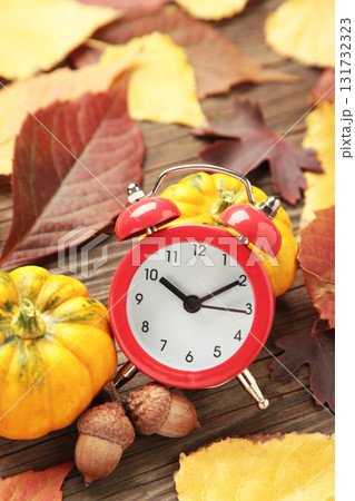 Red alarm clock, acorns and autumn leaves on grey wooden background. Daylight saving time end Red alarm clock, acorns and autumn leaves on grey wooden background. Daylight saving time end 131732323