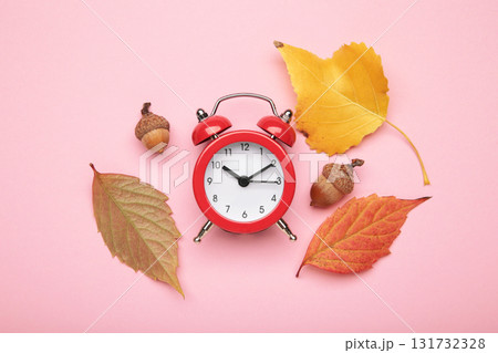 Red alarm clock, acorns and autumn leaves on pink background. Daylight saving time end Red alarm clock, acorns and autumn leaves on pink background. Daylight saving time end 131732328