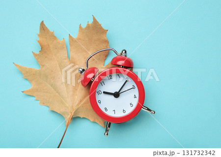 Red alarm clock and autumn leaves on blue background. Daylight saving time end Red alarm clock and autumn leaves on blue background. Daylight saving time end 131732342