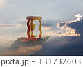 Hourglass held in hand against a dramatic sky backdrop. 131732603