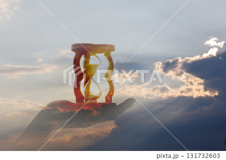 Hourglass held in hand against a dramatic sky backdrop. Hourglass held in hand against a dramatic sky backdrop. 131732603