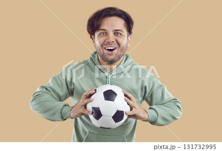 Soccer fan happy excited young man holding football ball in hands on beige background. Soccer fan happy excited young man holding football ball in hands on beige background. 131732995