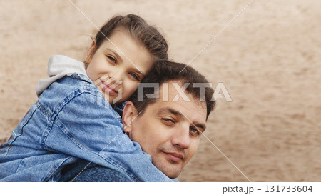 Happy daughter hugs dad from behind, side view on sandy beach Happy daughter hugs dad from behind, side view on sandy beach 131733604