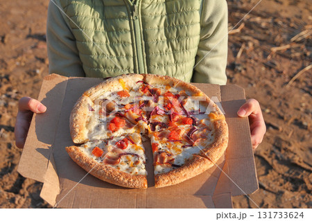 Unrecognizable child holding pizza paper box on beach in sunset light 131733624