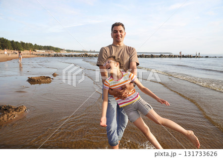 Happy dad twirls his laughing daughter on beach on sunny summer day 131733626