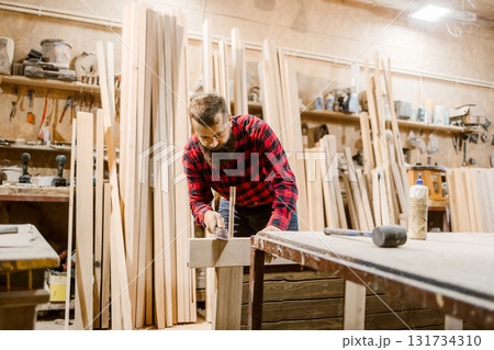 Carpenter working diligently in a woodworking shop on a rustic project surrounded by timber 131734310