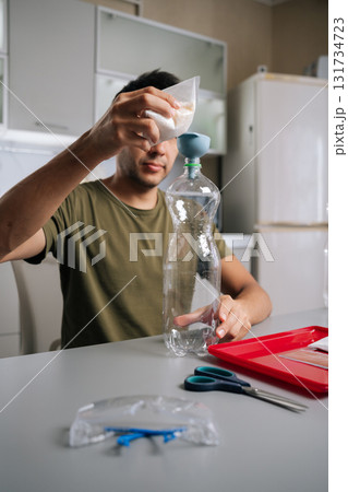 Vertical portrait of gardener male pouring fertilizer from bag into plastic bottle using funnel, preparing nutrients for plants, demonstrating sustainable approach to gardening and plant care. Vertical portrait of gardener male pouring fertilizer from bag into plastic bottle using funnel, preparing nutrients for plants, demonstrating sustainable approach to gardening and plant care. 131734723