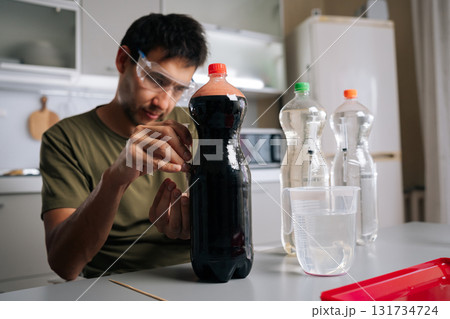 Focused chemist wearing protective eyewear mixing plant fertilizer solutions, handling precise syringes and chemical containers in professional laboratory setting. Concept of urban farming. 131734724
