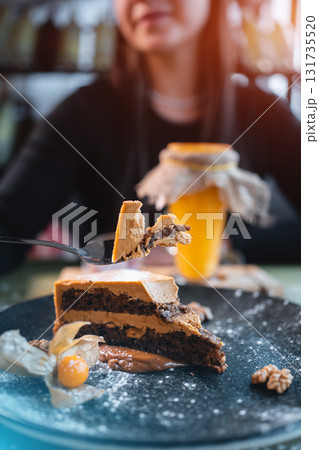 female eating chocolate nut cake with walnut and physalis on black plate in cafe female eating chocolate nut cake with walnut and physalis on black plate in cafe 131735520