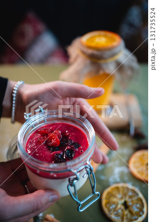 closeup of hand with berry panna cotta dessert and red cherry sauce in glass jar 131735524