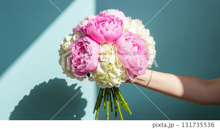 A hand holds a beautiful, elegant bouquet of fresh flowers against a bright, light blue background. 131735536