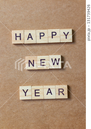 Wooden letter tiles arranged to spell HAPPY NEW YEAR on a brown textured background 131739426