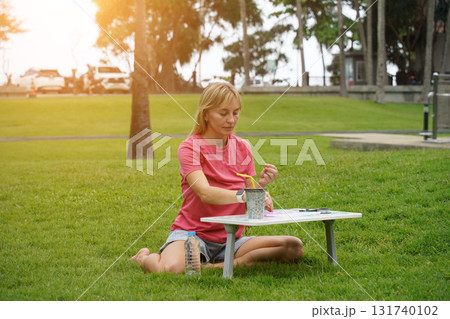 Young woman beading colorful bracelets outdoors in a park 131740102
