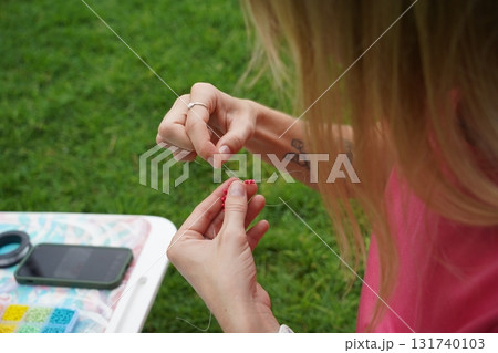 Young woman beading colorful bracelets outdoors in a park Young woman beading colorful bracelets outdoors in a park 131740103