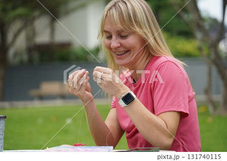 Young woman beading colorful bracelets outdoors in a park 131740115