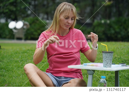 Young woman beading colorful bracelets outdoors in a park Young woman beading colorful bracelets outdoors in a park 131740117